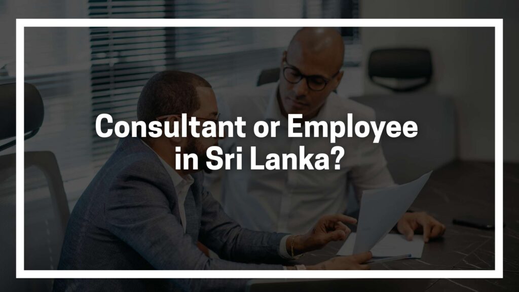 Two individuals seated at a desk in a modern office setting, reviewing documents together. The text overlay reads: “Consultant or Employee in Sri Lanka?” indicating a discussion about employment classification.
