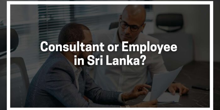 Two individuals seated at a desk in a modern office setting, reviewing documents together. The text overlay reads: “Consultant or Employee in Sri Lanka?” indicating a discussion about employment classification.